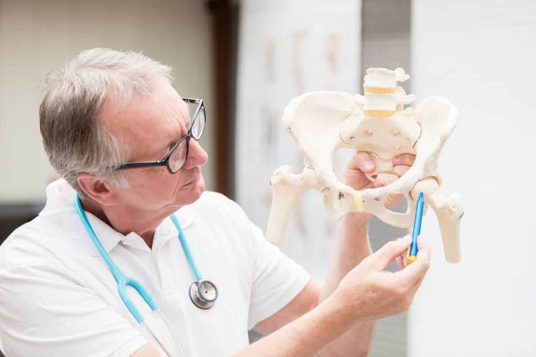 Doctor explaining iliopsoas bursitis by pointing to hip joint on anatomical model.
