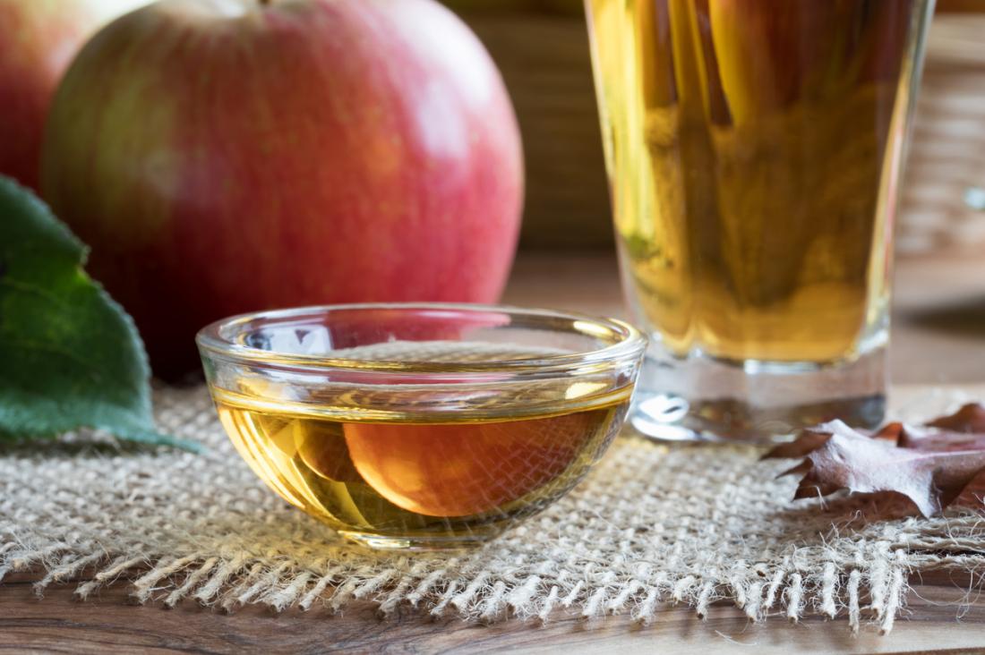 Apple cider vinegar in glass and bowl, next to large apple on table.