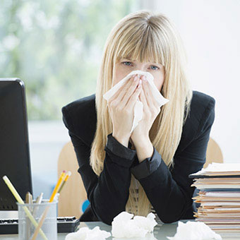 A woman sick at work blows her nose.