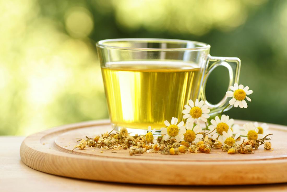 A mug of chamomile herbal tea, surrounded by chamomile plants and flowers.