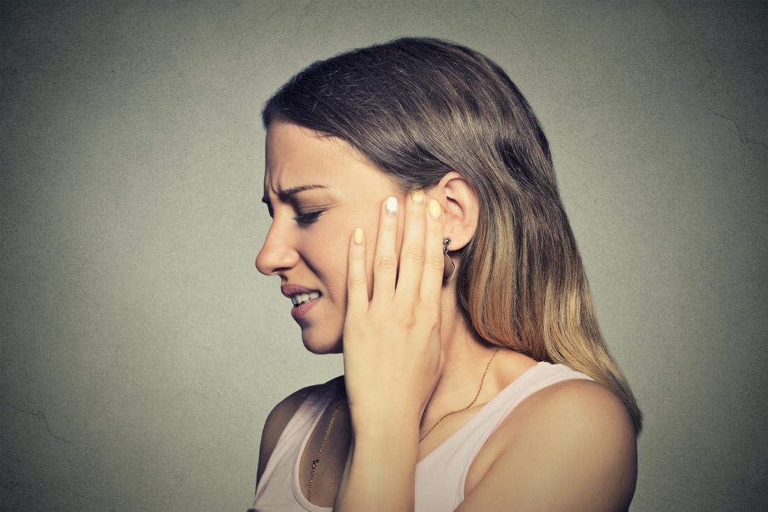 Woman holding her left ear in pain because of an infection.