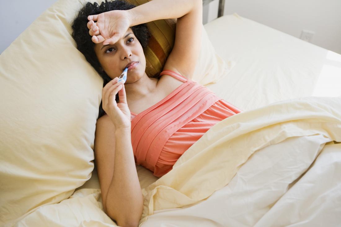 Woman with a fever measuring her temperature in bed