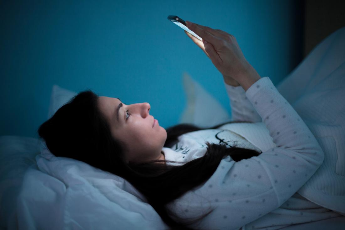 woman in bed staying up late looking at smart phone