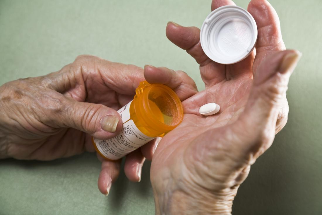 Person with arthritis, with medicine pill in palm from prescription drug pot.
