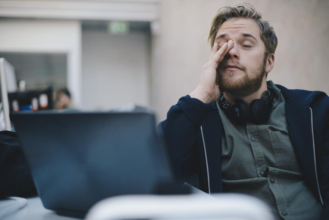 Tired or fatigued man rubbing eyes during stressful day at work