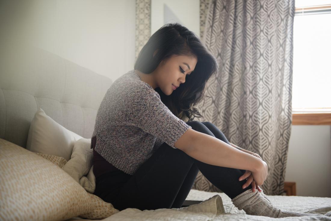 Depressed woman dealing with infertility issues sitting on bed holding knees