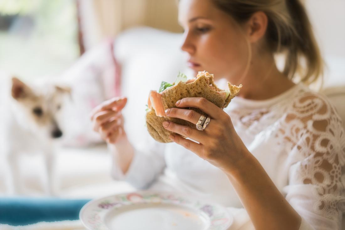 Woman experiencing compulsive eating before period holding a sandwich