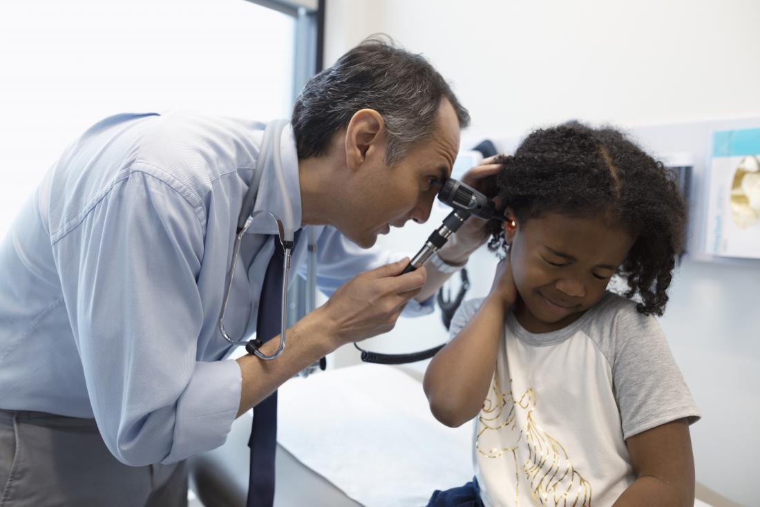 Pediatrician or doctor inspecting ear of upset child in office