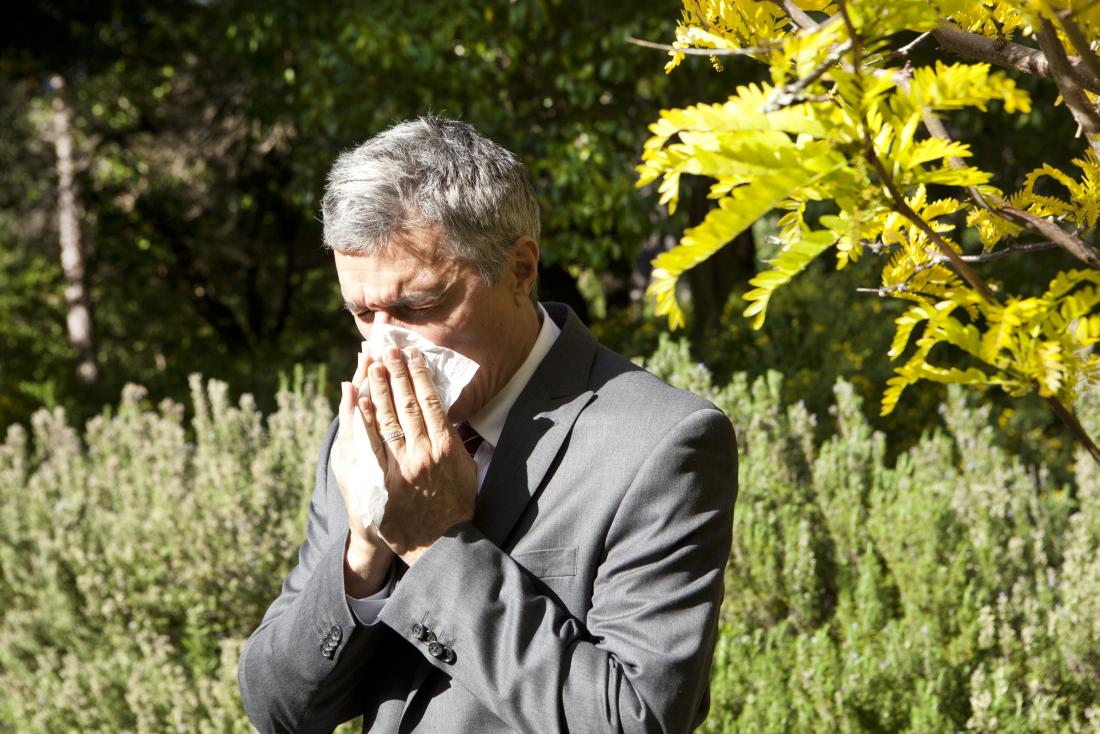 Man blowing his nose outdoors because of pollen allergy.