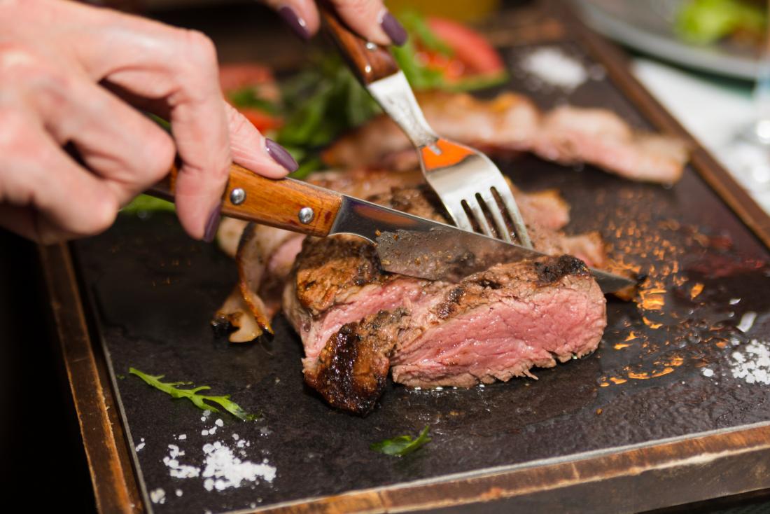 two hands cutting red meat with knife and fork