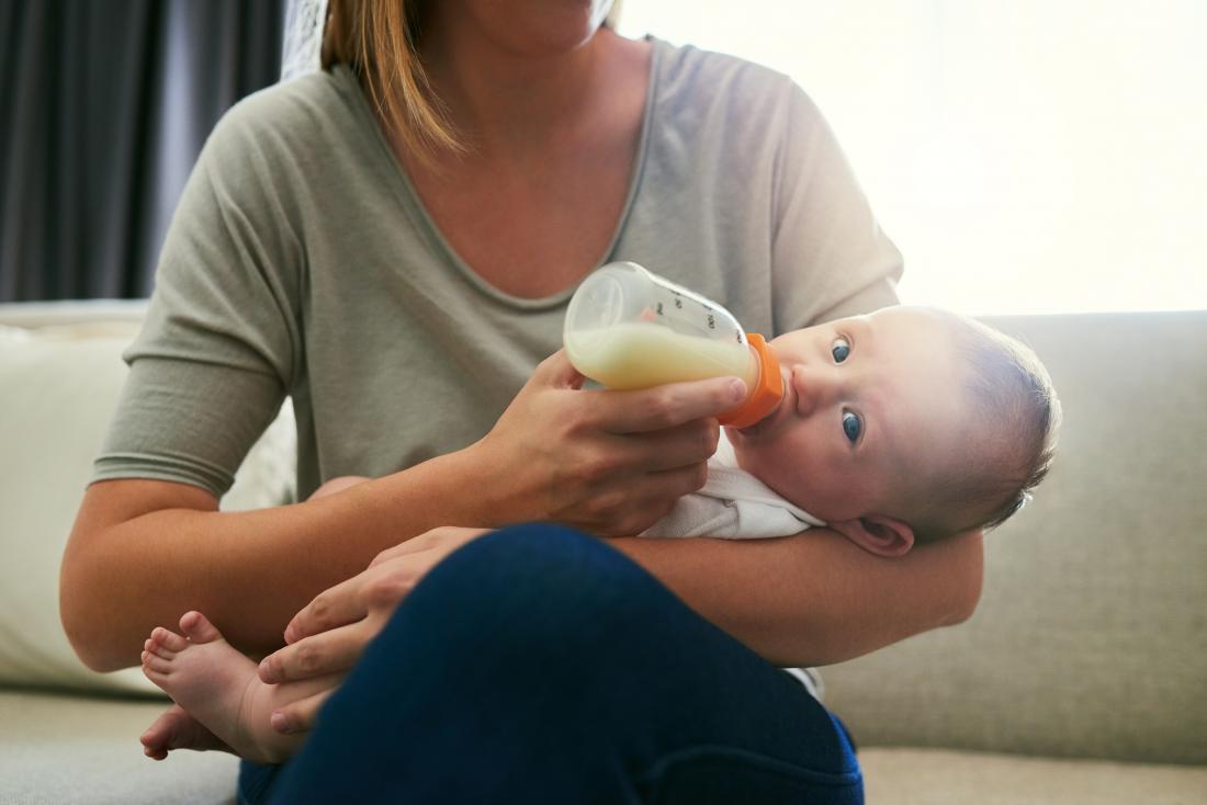 Mother feeding baby in her arms with milk bottle.