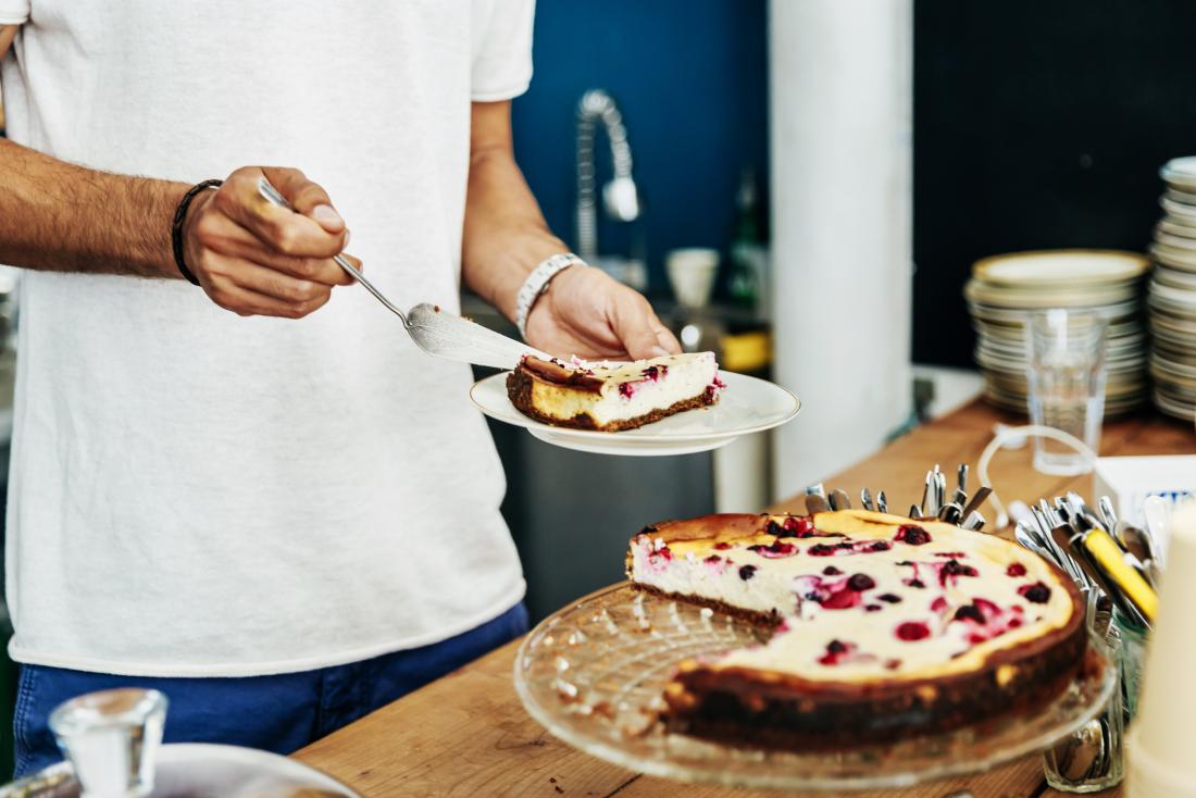 Man taking slice of cake onto plate in kitchen