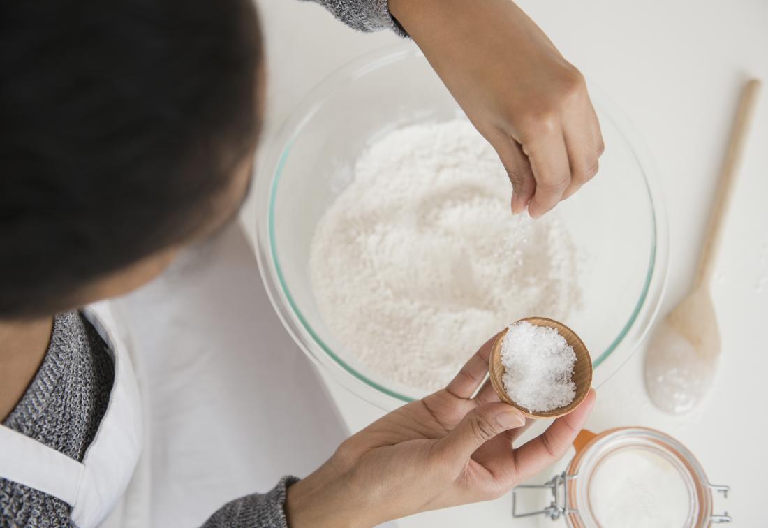 Top down view of woman sprinkling sugar or coconut into bowl of flour while baking