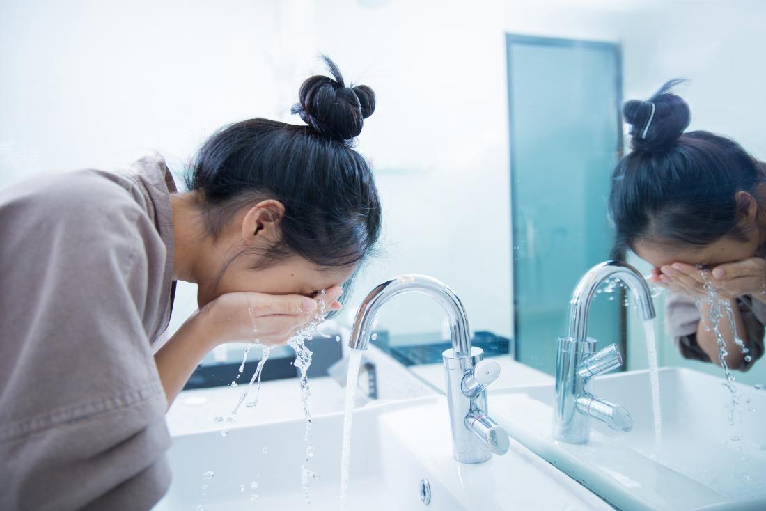 Woman washing her face in sink.