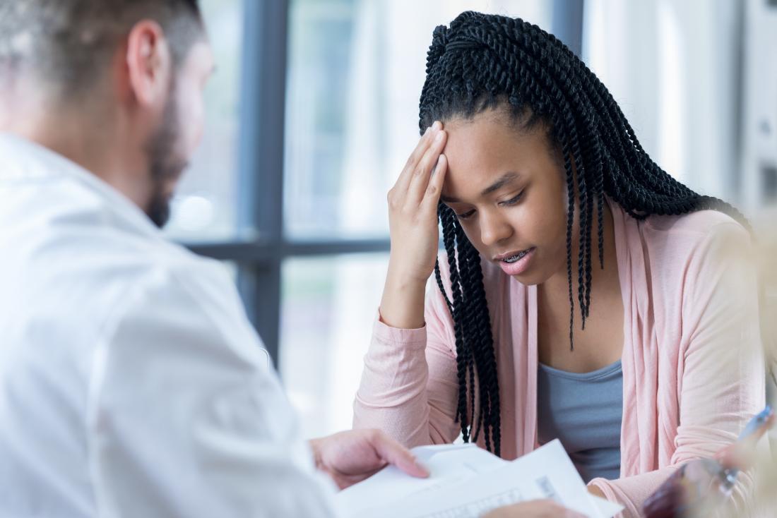 Young woman with headache speaking to doctor.