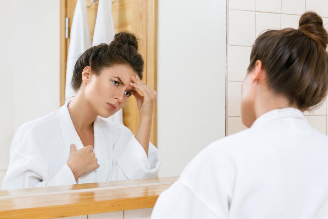 Woman with chest pain and headache looking in bathroom mirror in dressing gown