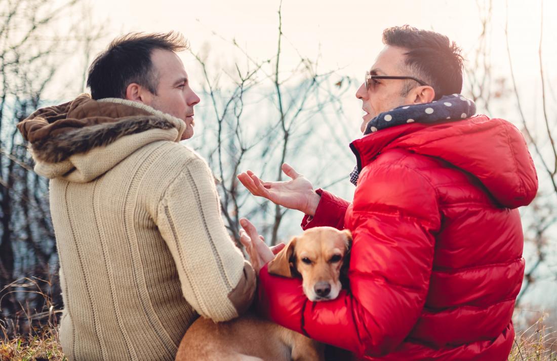 Two men talking outdoors with dog in winter coats