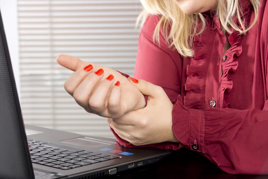Woman working on laptop holding her wrist because of repetitive strain injury.