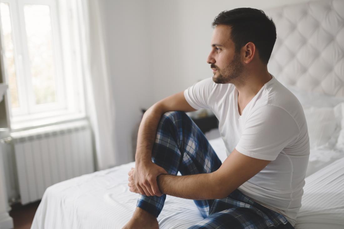 Man sitting on a bed looking contemplative, suffering from erectile dysfunction, or ed.