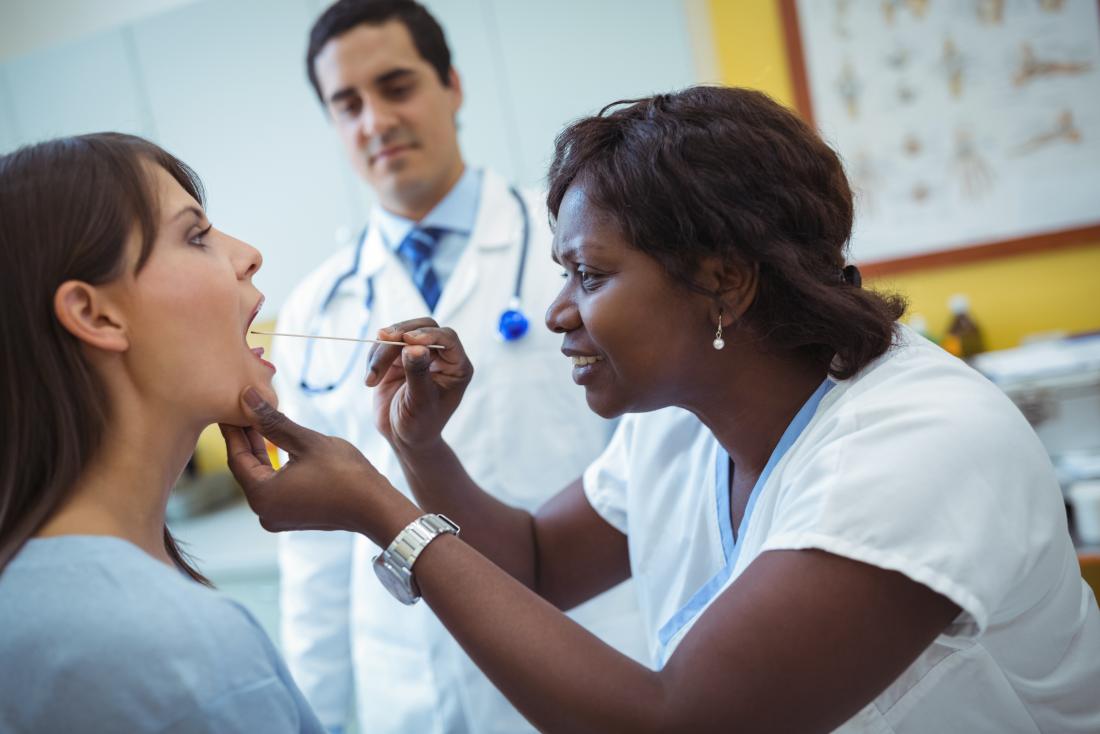 Doctor inspecting patients throat with another doctor, using tongue decompressor.