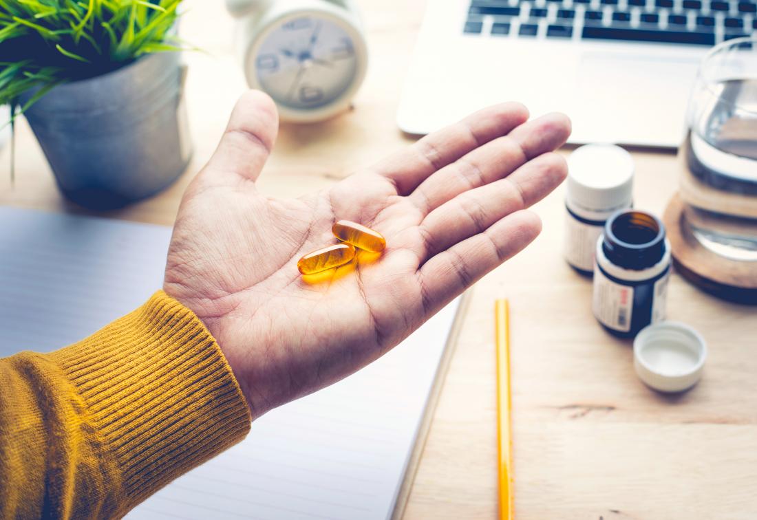 Person at desk holding omega-3 supplements in palm