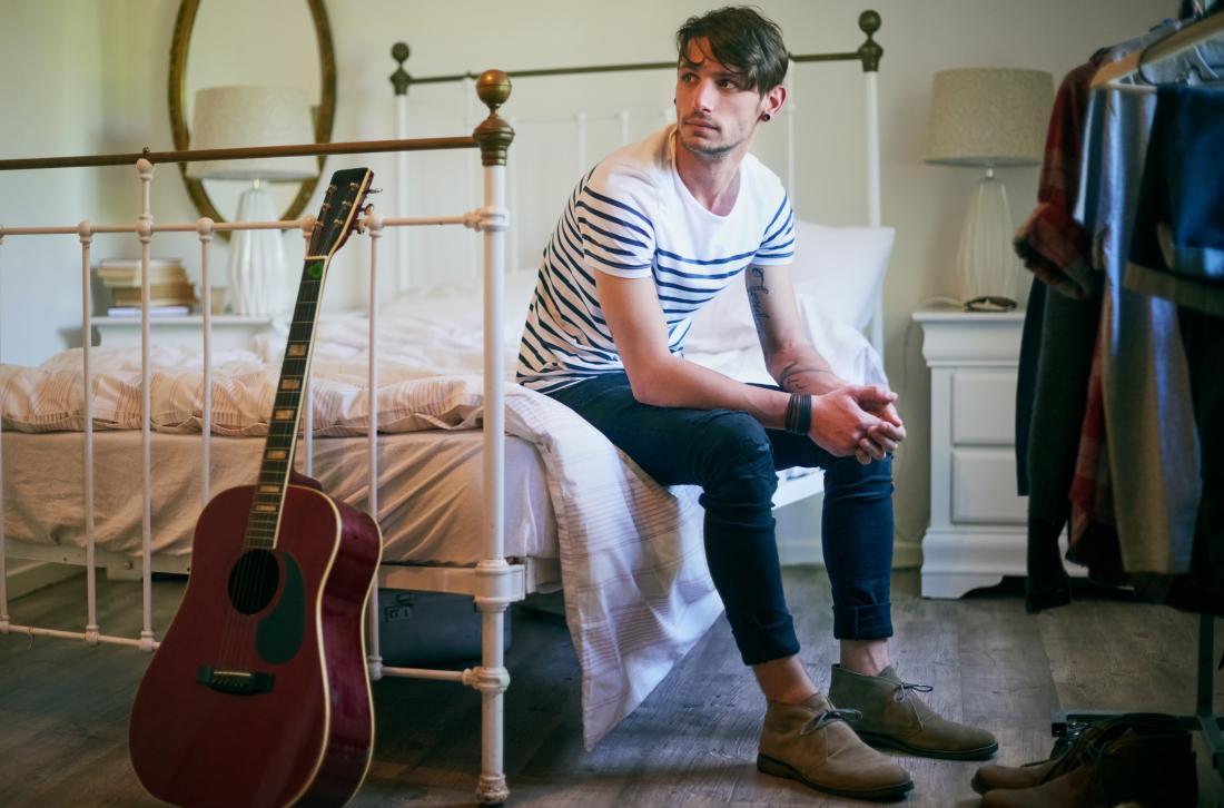 Man sitting on bed in bedroom with guitar and wardrobe