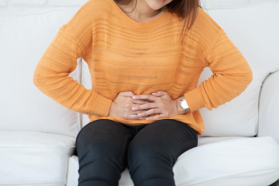 woman sitting on sofa holding stomach