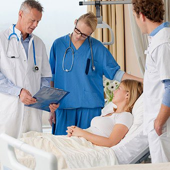 A group of doctors and nurses consulting with patient in a hospital room.