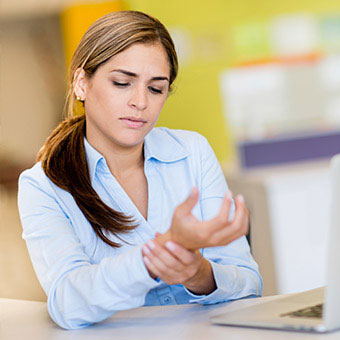 A young woman suffering from carpal tunnel holds her wrist in pain.