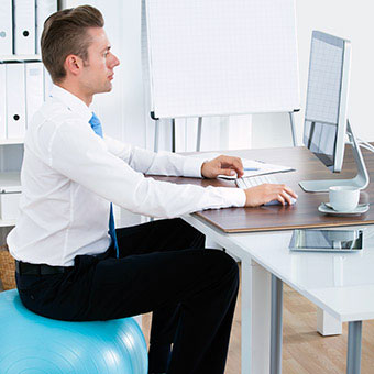 A businessman sits on a yoga ball at his desk to improve posture.