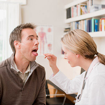 A doctor examines the throat of an infected patient looking for redness and enlargement of the tonsils.