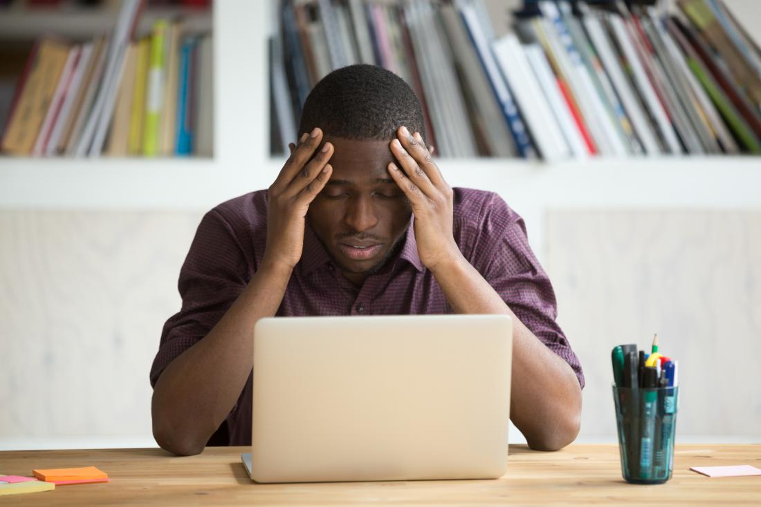 Frustrated man with his head in his hands in front of his laptop