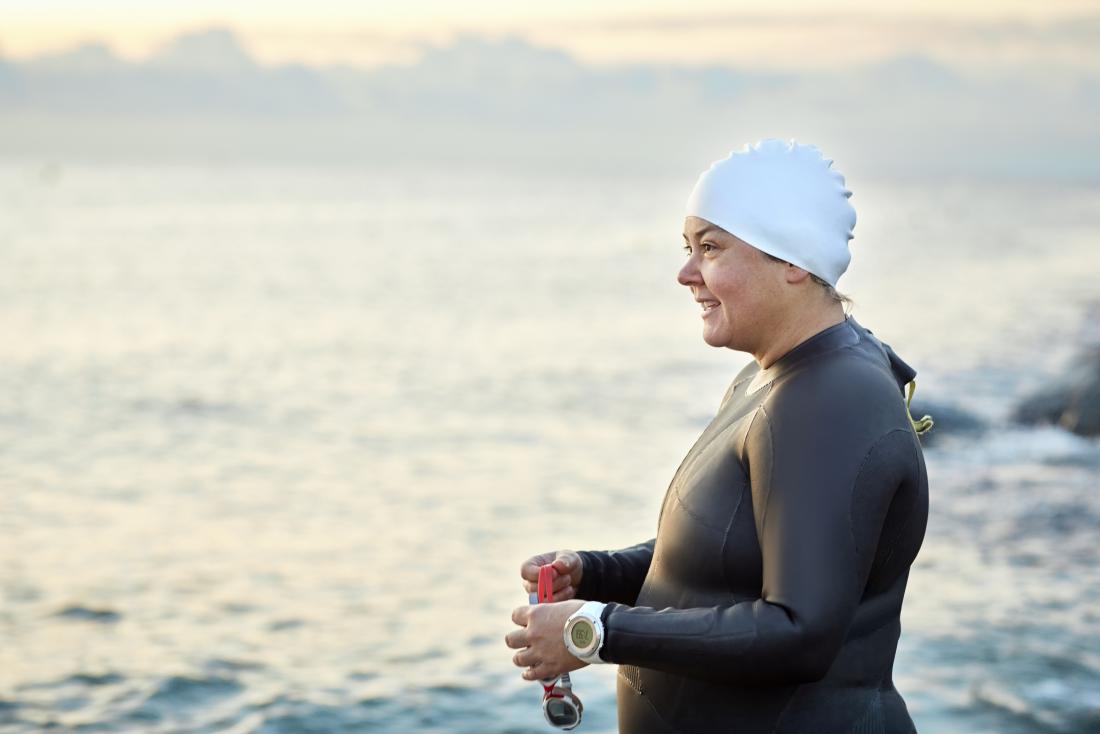 Woman athlete by the sea in outdoor swimmer wetsuit, going swimming.