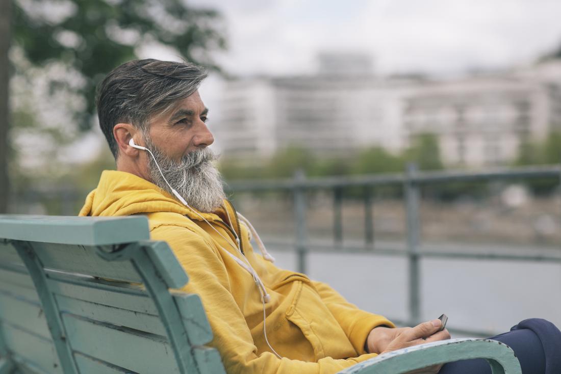 Mature man sitting on bench listening to music.