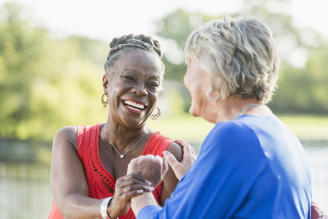 Two older female friends laughing together in a park.