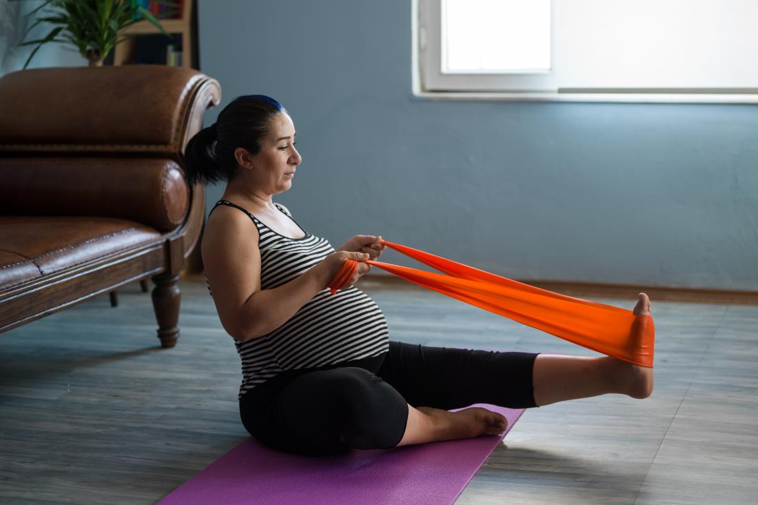 Pregnant woman stretching foot and leg with towel or exercise band