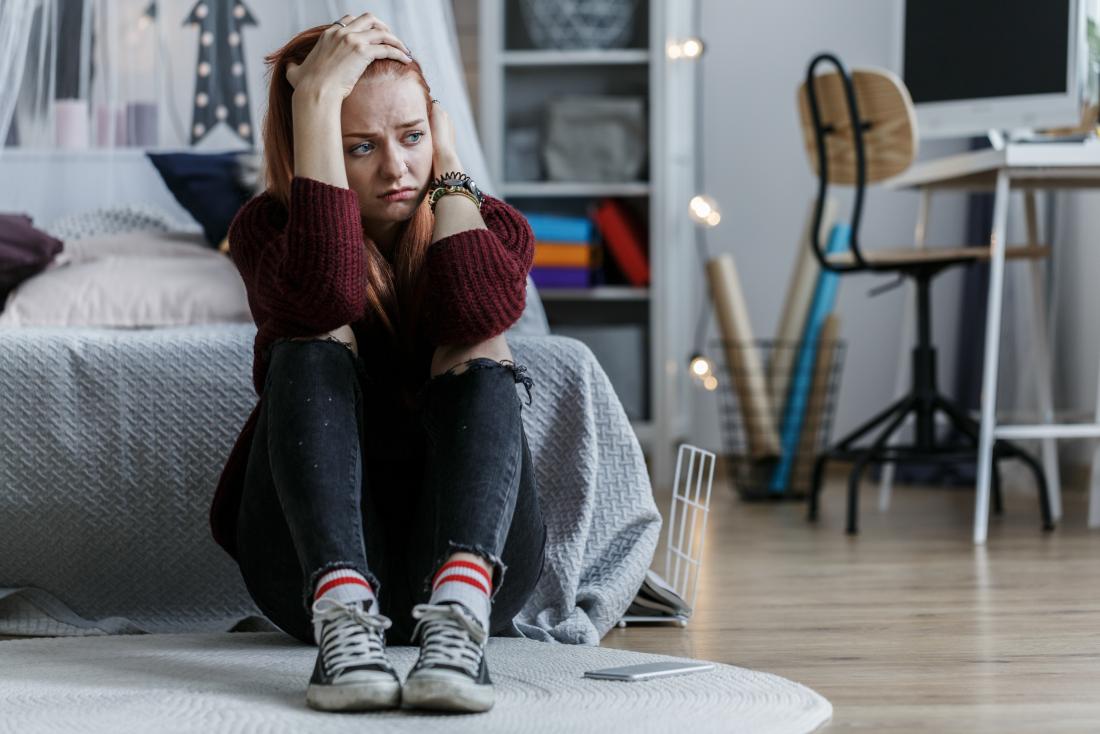 Depressed and worried young woman sitting on floor in bedroom looking sad