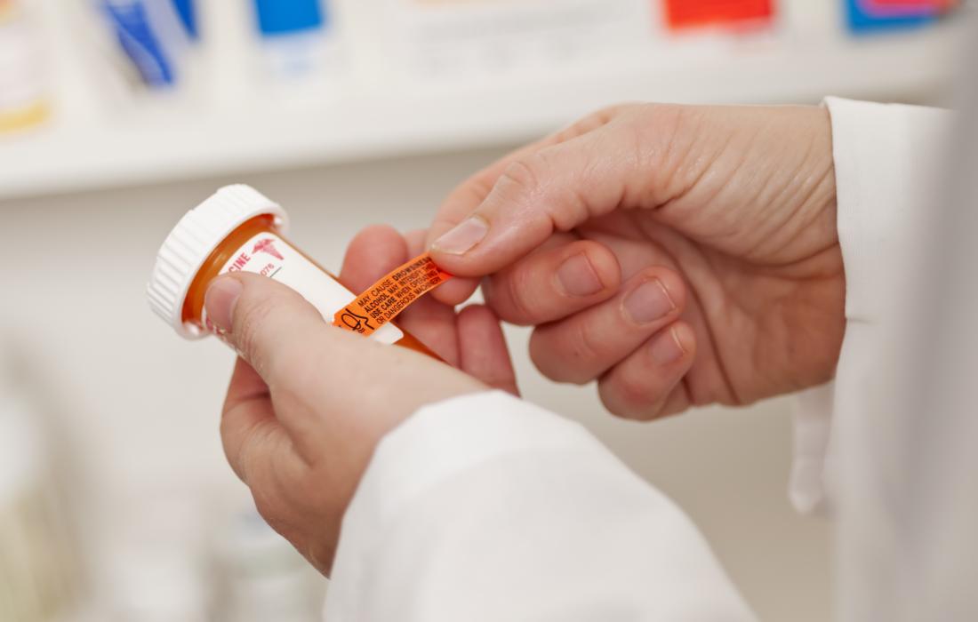 Pharmacist applying label to prescription pill bottle