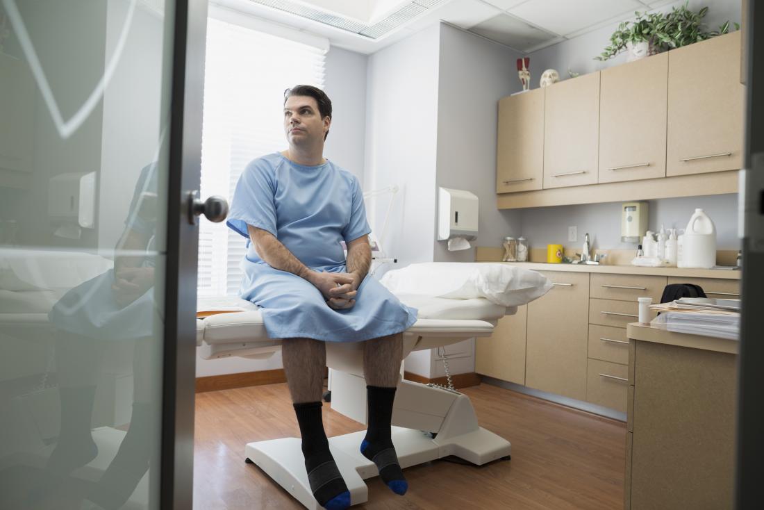 Man in hospital gown sitting on bed in doctor's office waiting to be tested for chlamydia in men