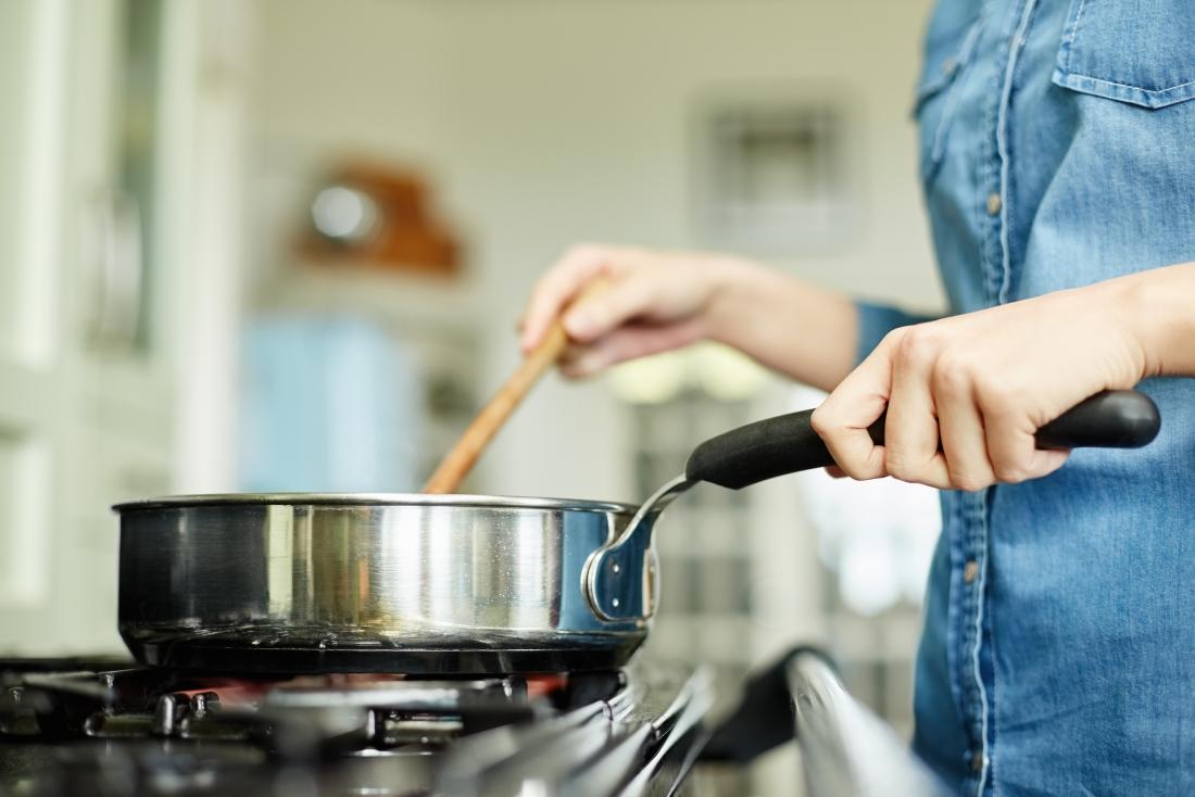 Person holding pan handle while cooking in kitchen