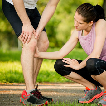 A female runner helps a male runner experiencing knee pain.