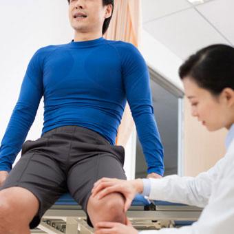 A doctor examines a male patient with knee pain.