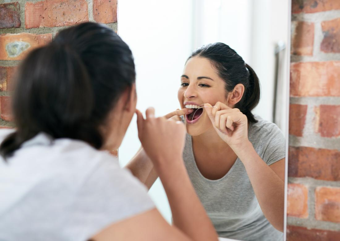 Woman flossing in the mirror to remove plaque