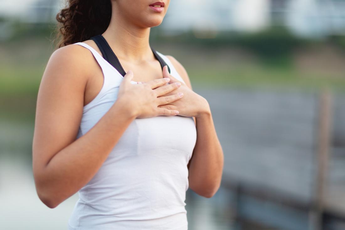 Woman holding hands to chest in pain while outdoors in running clothes