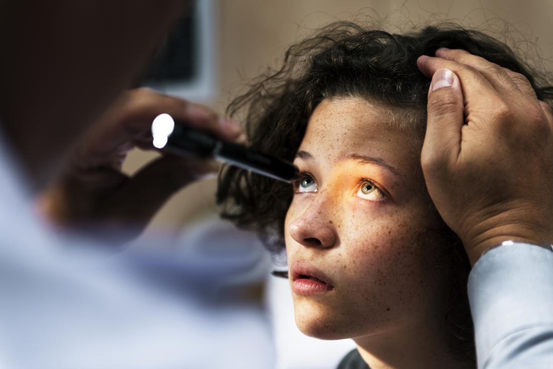 Person having torch shone into eye by doctor for eye exam