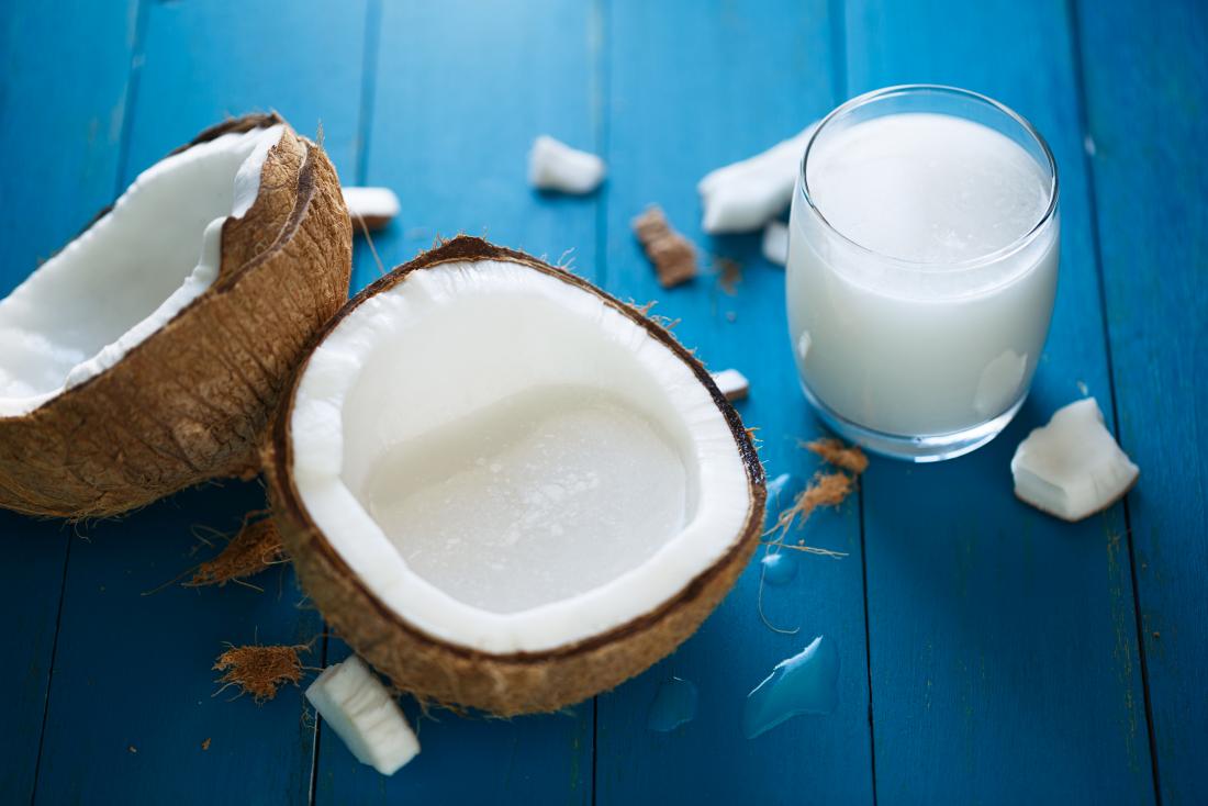 halved coconut on blue wooden tabletop with glass of coconut milk