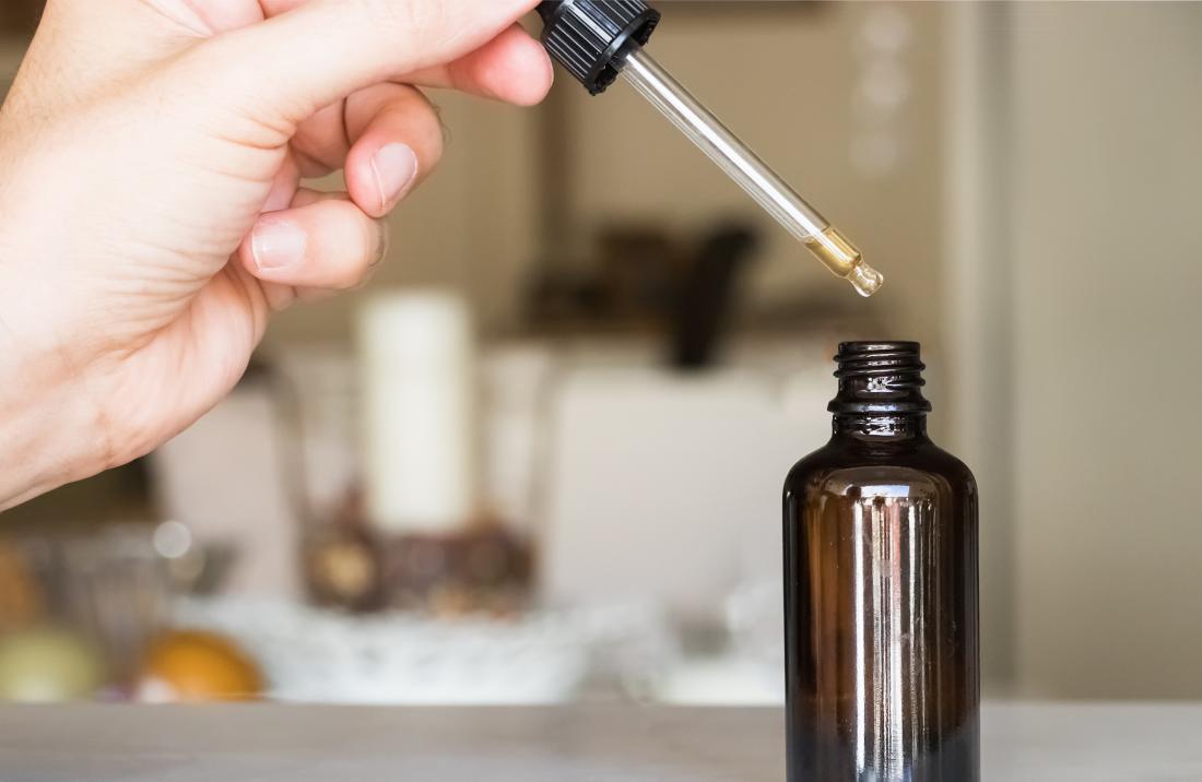Person using dropper of essential oil from glass bottle.