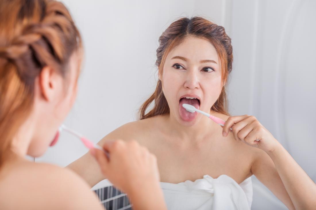 A woman brushes her tongue in front of the mirror to prevent tonsil stones.