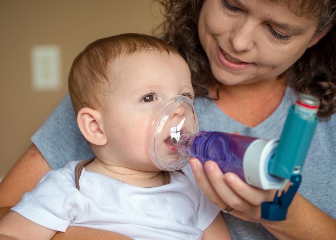 mother using an asthma inhaler with mask attachment on baby