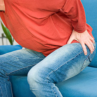 A man experiences lower back and buttock pain while trying to stand up from a seated position.